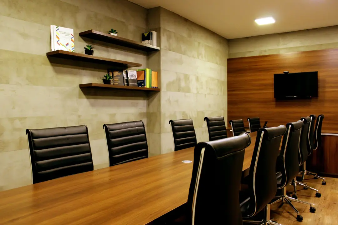 Sala de reuniões corporativa com mesa de madeira, cadeiras executivas em couro preto e parede com detalhe em madeira