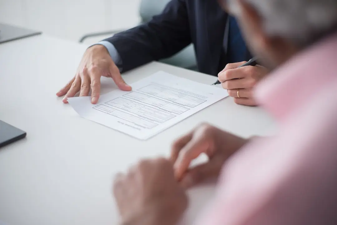 Mãos de profissional e cliente analisando documento sobre mesa branca durante reunião de consultoria